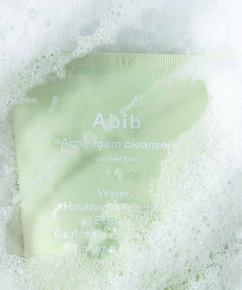 ABIB Acne Foam Cleanser with Mugwort Foam 250ml in a green tube covered in white foam, showcasing its cleansing properties.