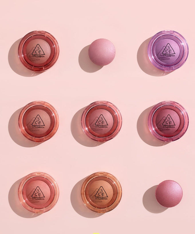Assorted 3CE Bouncy Blur Balm compacts in various shades on a pink background, highlighting makeup products.