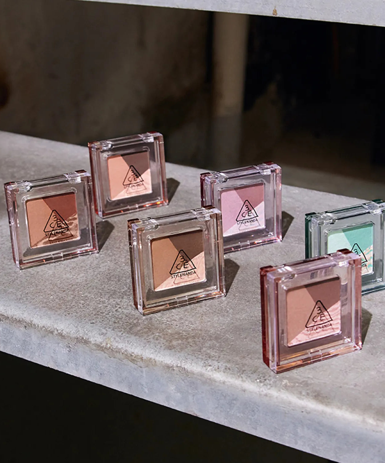 Six 3CE Color Grid Eyeshadow palettes displayed on a stone surface showcasing various shades.