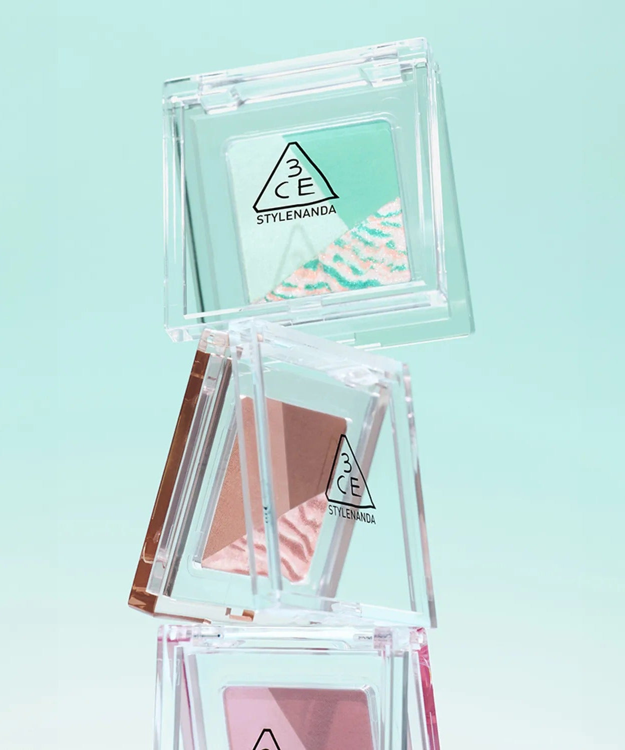 Stack of 3CE Color Grid Eyeshadow palettes with various shades on a light green background