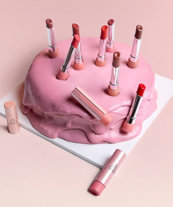 Collection of 3CE Glaze Lip Glow 3.2g lipsticks in various shades arranged creatively on a pink frosted cake.