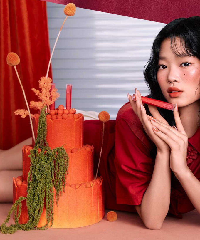 Model showcasing 3CE Velvet Lip Tint Plush with artistic floral background