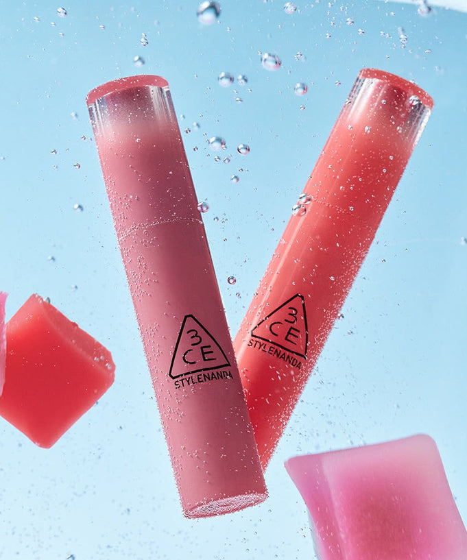 Two 3CE Lazy Pop Lip Stain tubes submerged in water, showcasing vibrant color and sleek packaging.
