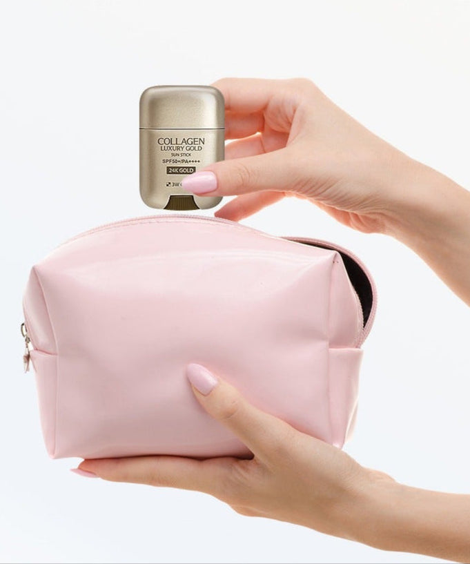 Hand holding 3W CLINIC Collagen & Luxury Gold Sun Stick 18g above a pink cosmetic bag