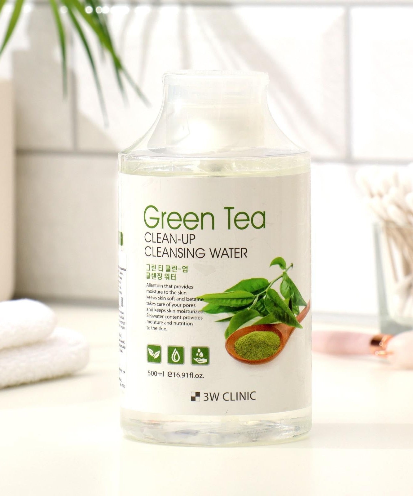 3W CLINIC Green Tea Clean Up Cleansing Water 500ml bottle on bathroom counter with plants and towels.