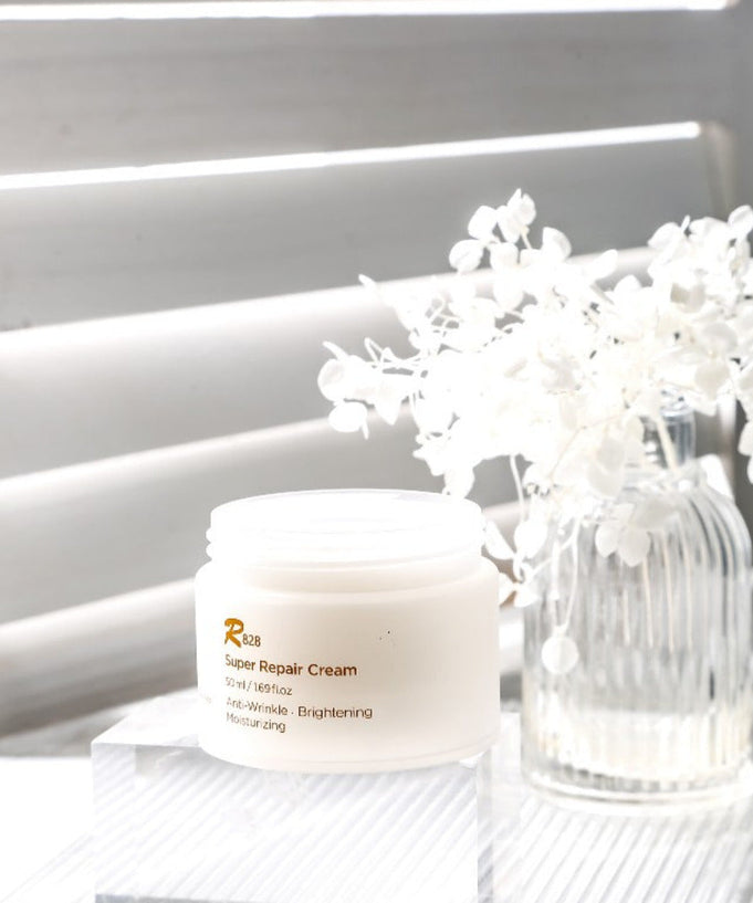 R828 Super Repaire Cream 50 ml displayed with a white floral arrangement in the background.