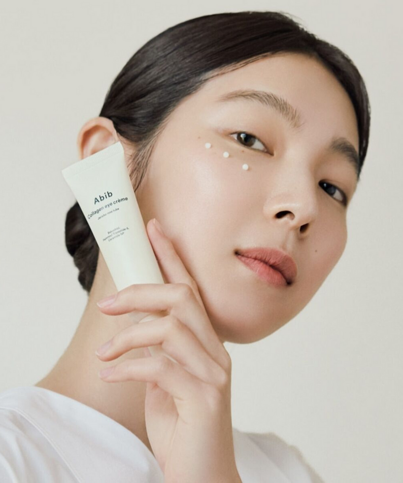 Model holding ABIB Collagen Eye Cream Resurrection Herb Tube 30ml against face, showcasing product application on skin.