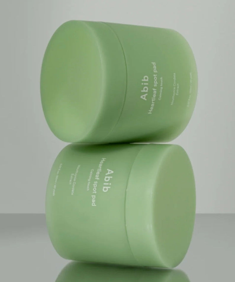 ABIB Heartleaf Spot Pad Calming Touch 70 pads displayed in green containers on a reflective surface.