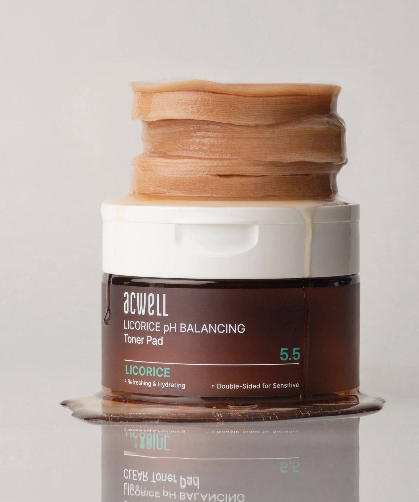 ACWELL Licorice pH Balancing Toner Pad 70P container with stack of pads and spilled liquid on reflective surface, front view.