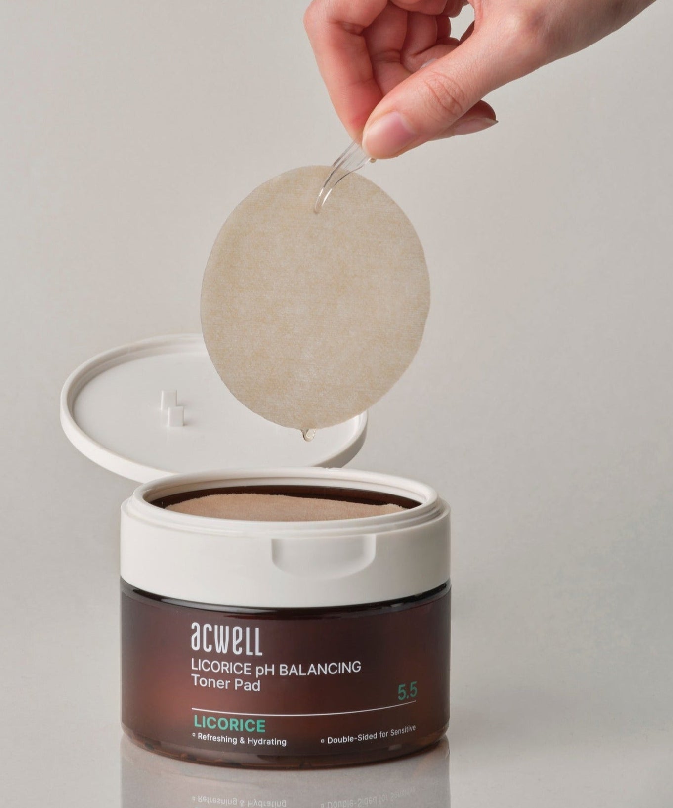Close-up of ACWELL Licorice pH Balancing Toner Pad 70P with a hand holding a toner pad above the open container.