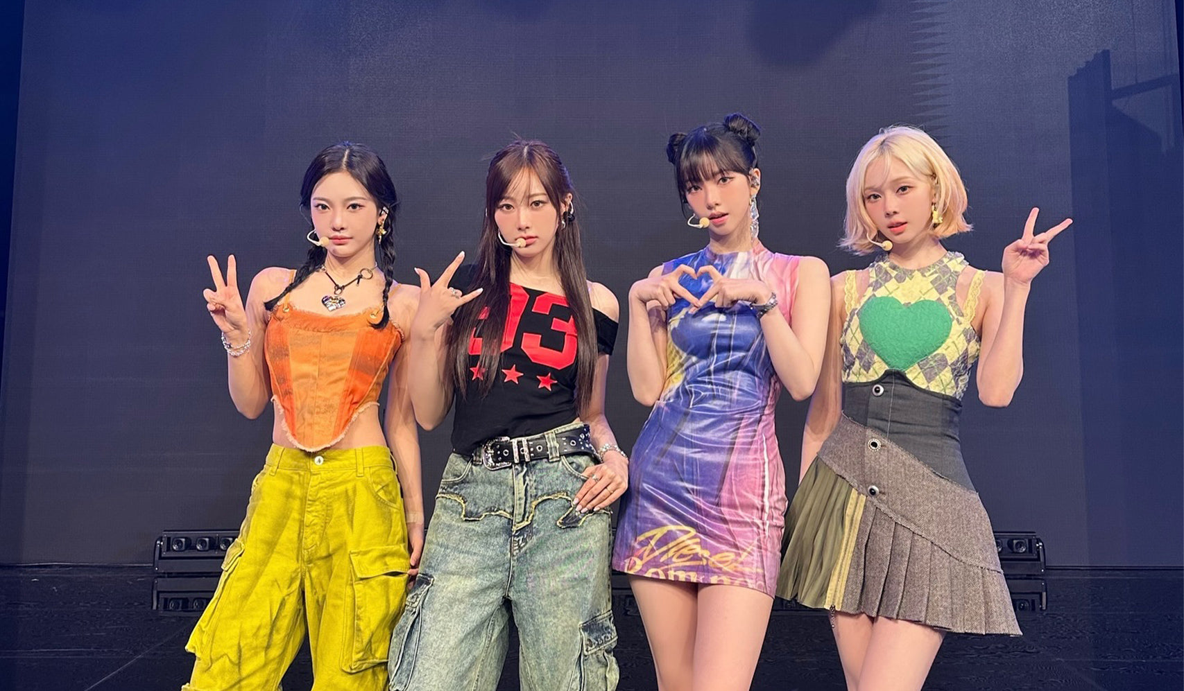 Four women posing together on stage, wearing fashionable outfits with vibrant colors and unique styles.