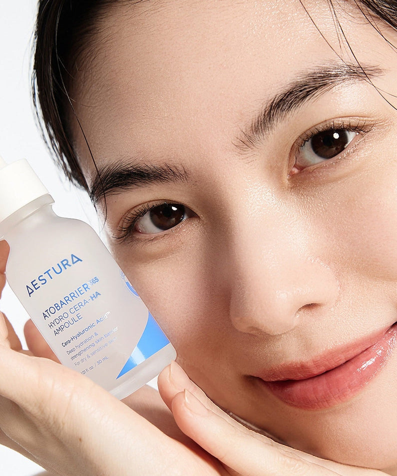 Smiling person holding AESTURA Atobarrier 365 Hydro Cera-HA Ampoule 30ml near face, showcasing the skincare product's hydrating benefits.