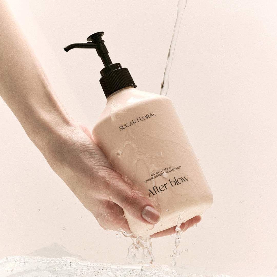Hand holding AFTER BLOW Perfume Hand Wash Sugar Floral 400ml bottle with water splash