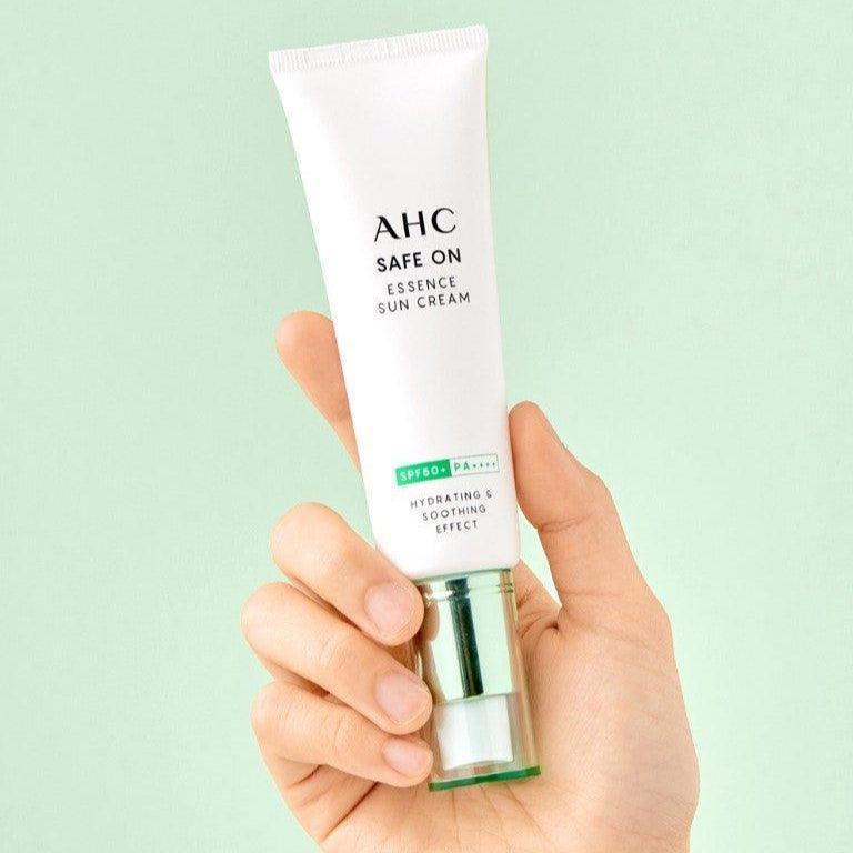 AHC Safe On Essence Sunscreen 50ml tube held in a hand against a mint green background.