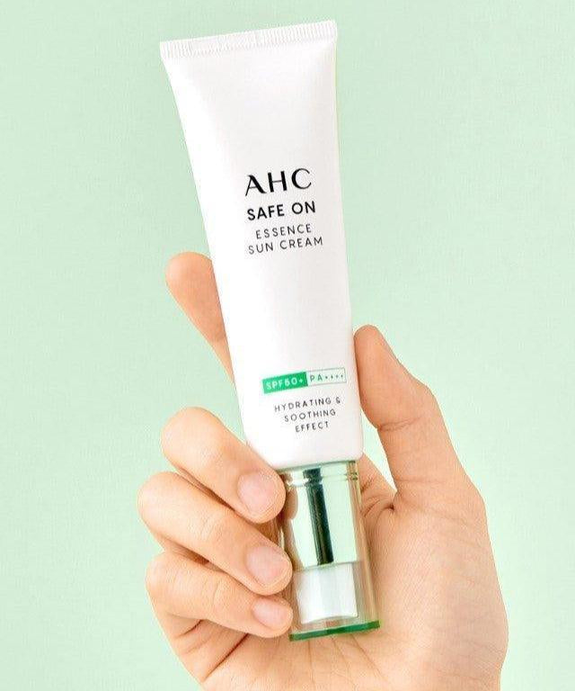 AHC Safe On Essence Sunscreen 50ml tube held in a hand against a mint green background.