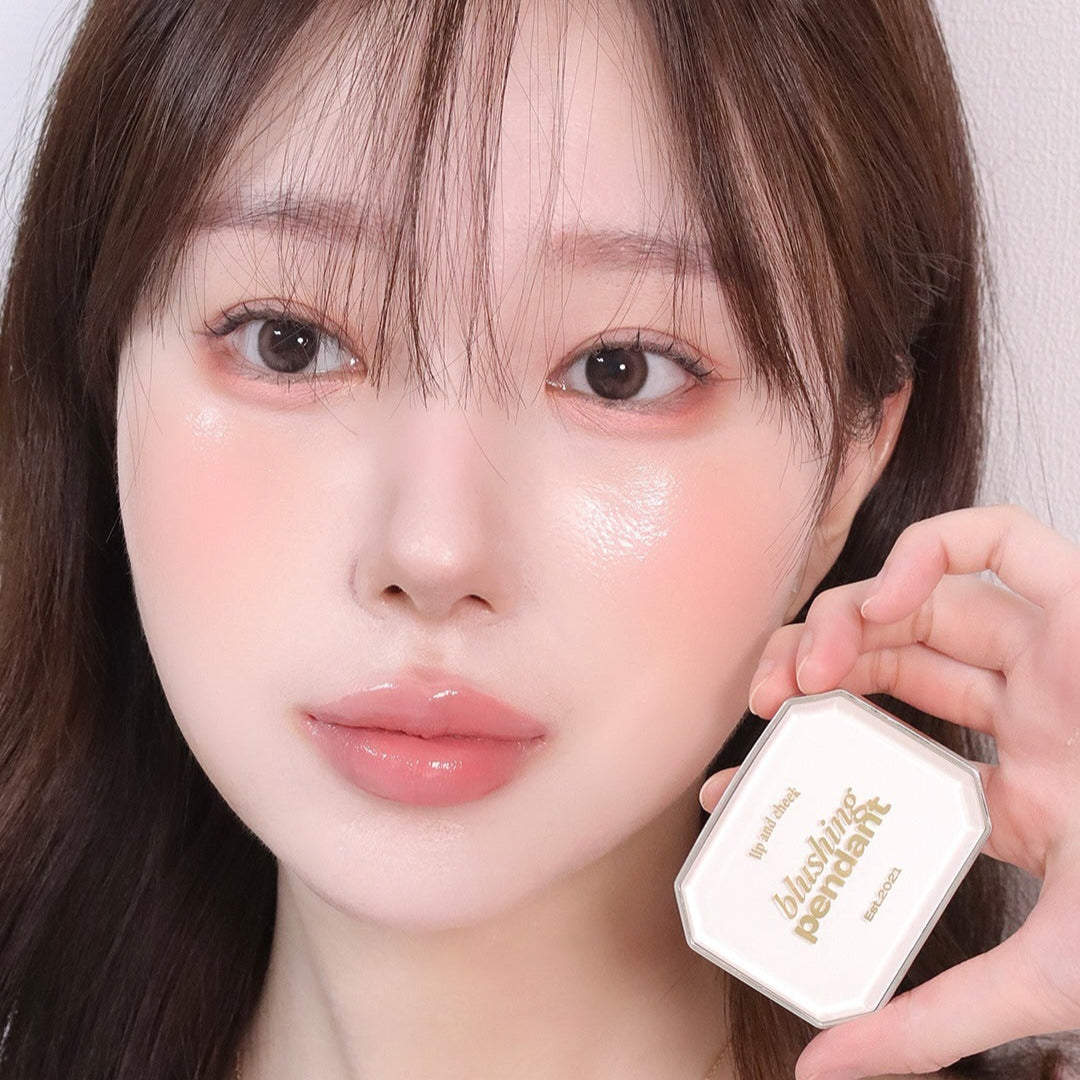 Woman holding ALTERNATIVE STEREO Blushing Pendant Lip & Cheeck with radiant makeup look.