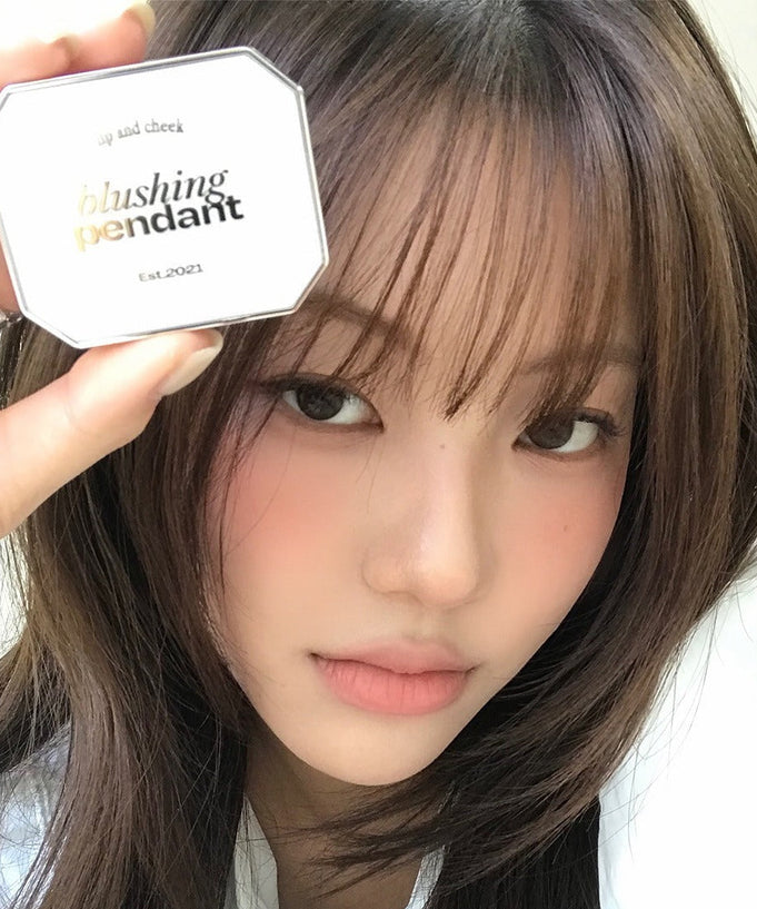 Woman holding ALTERNATIVE STEREO Blushing Pendant Lip & Cheeck product near her face.