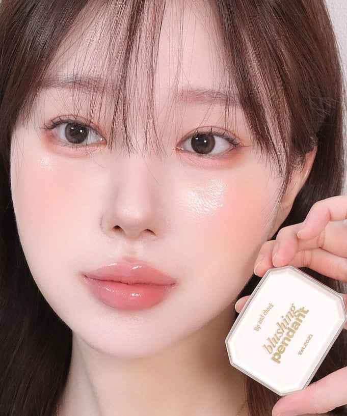 Woman holding ALTERNATIVE STEREO Blushing Pendant Lip & Cheeck with radiant makeup look.