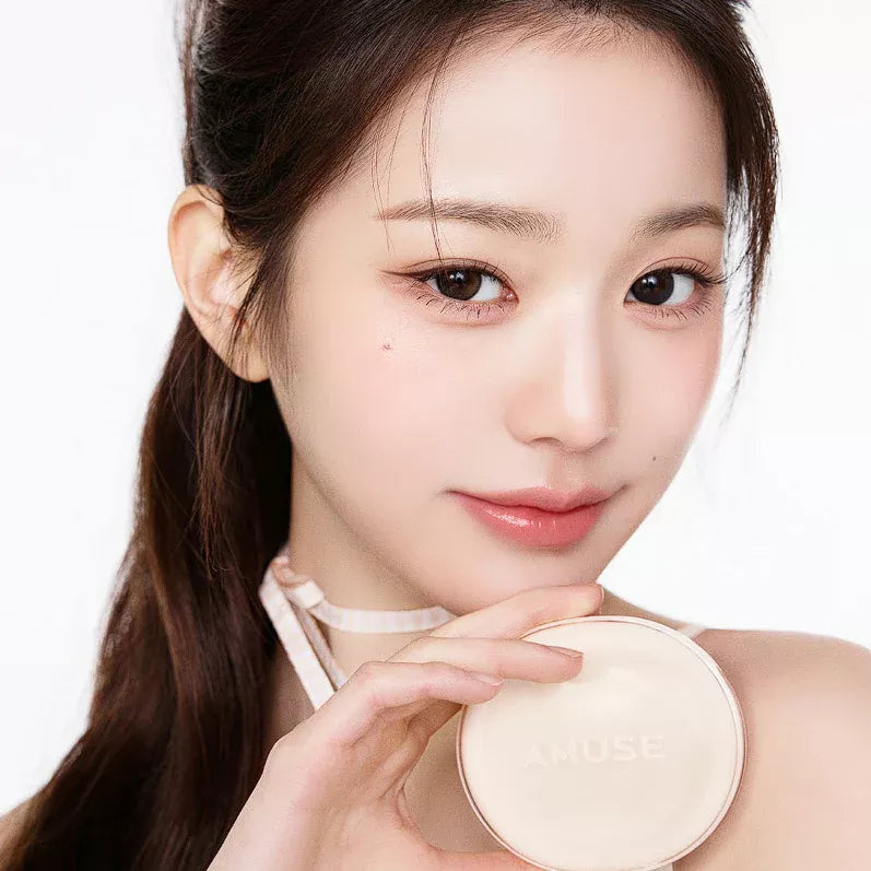 Woman holding AMUSE Dew Jelly Master Cushion in hand against a light background, showcasing the product's packaging