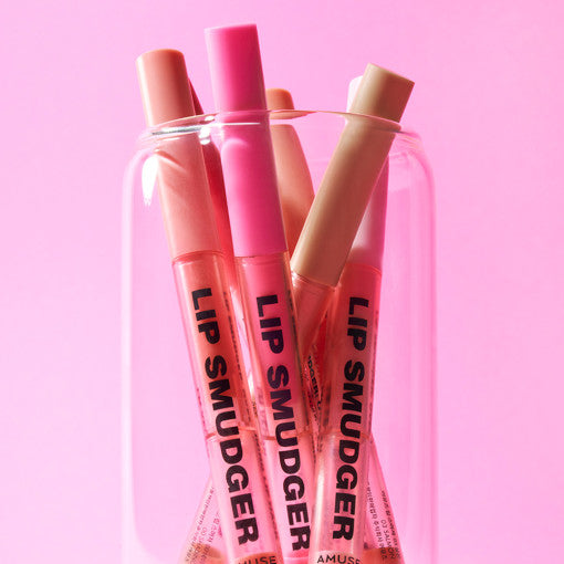 Assorted AMUSE Lip Smudger pens in a glass jar on a pink background.
