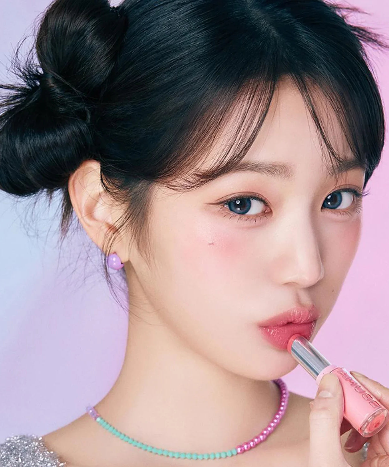 Woman applying AMUSE Fondue Balm with a pink background, showcasing the lipstick's color and texture.