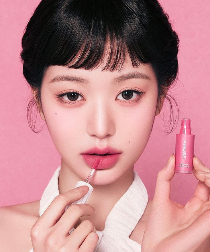 Model applying AMUSE Powder Velvet Tint, showcasing product texture and color.