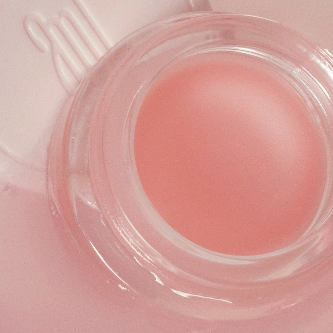 ANILLO Mellow Glow Balm in a clear container with a pink hue, offering moisturizing benefits and enhancing skin's natural glow.