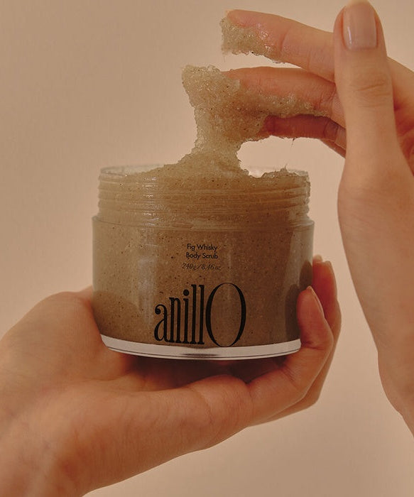 Hands holding an open jar of ANILLO Fig Whisky Body Scrub 240g with scrub texture visible.
