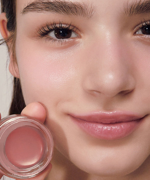 Woman holding a jar of ANILLO Rose Glow Balm with a subtle pink tint on her lips.