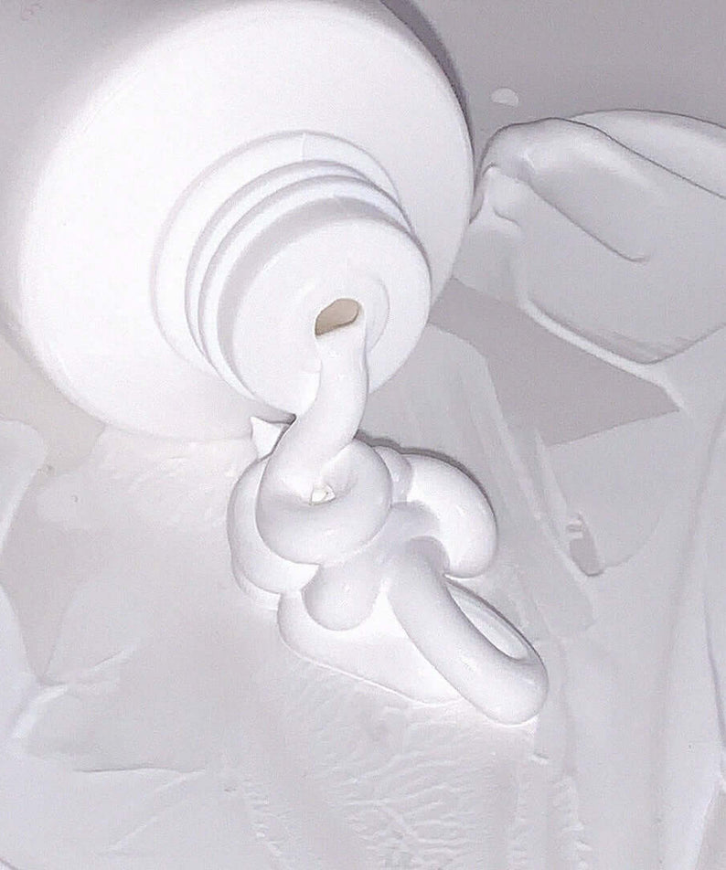 AOU Tone-Up Dazzling Cream spread out from an open tube, showcasing its texture and smoothing properties.