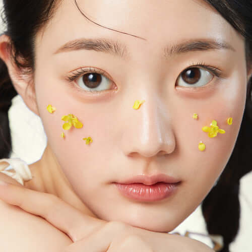 Young woman with flower petals on cheek using APRILSKIN Calendula Hyaluronic Toner Pad for skincare.