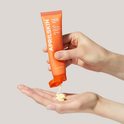 Person applying APRILSKIN Carrotene Clearifying Cream from an orange tube onto their hand.