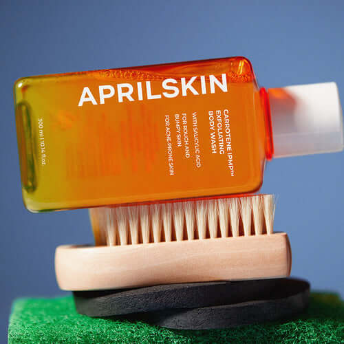 APRILSKIN Carrotene IPMP Exfoliating Body Wash with exfoliating brush on a green background