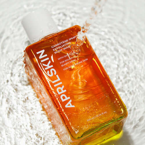 Orange bottle of APRILSKIN Carrotene IPMP Exfoliating Body Wash on a watery surface