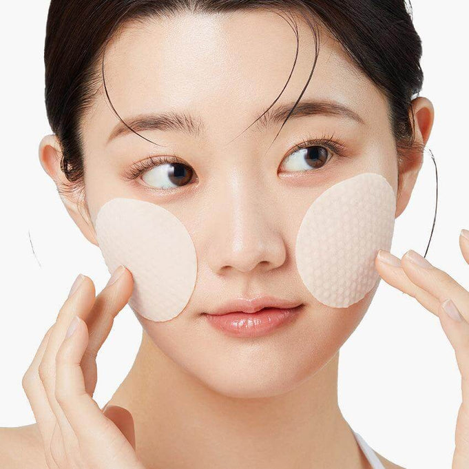 Woman applying skincare pads to her cheeks for a facial treatment.