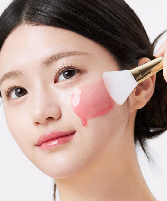 Woman applying APRILSKIN TXA Niacinamide 99 Night Wrapping Mask 80ml with brush.