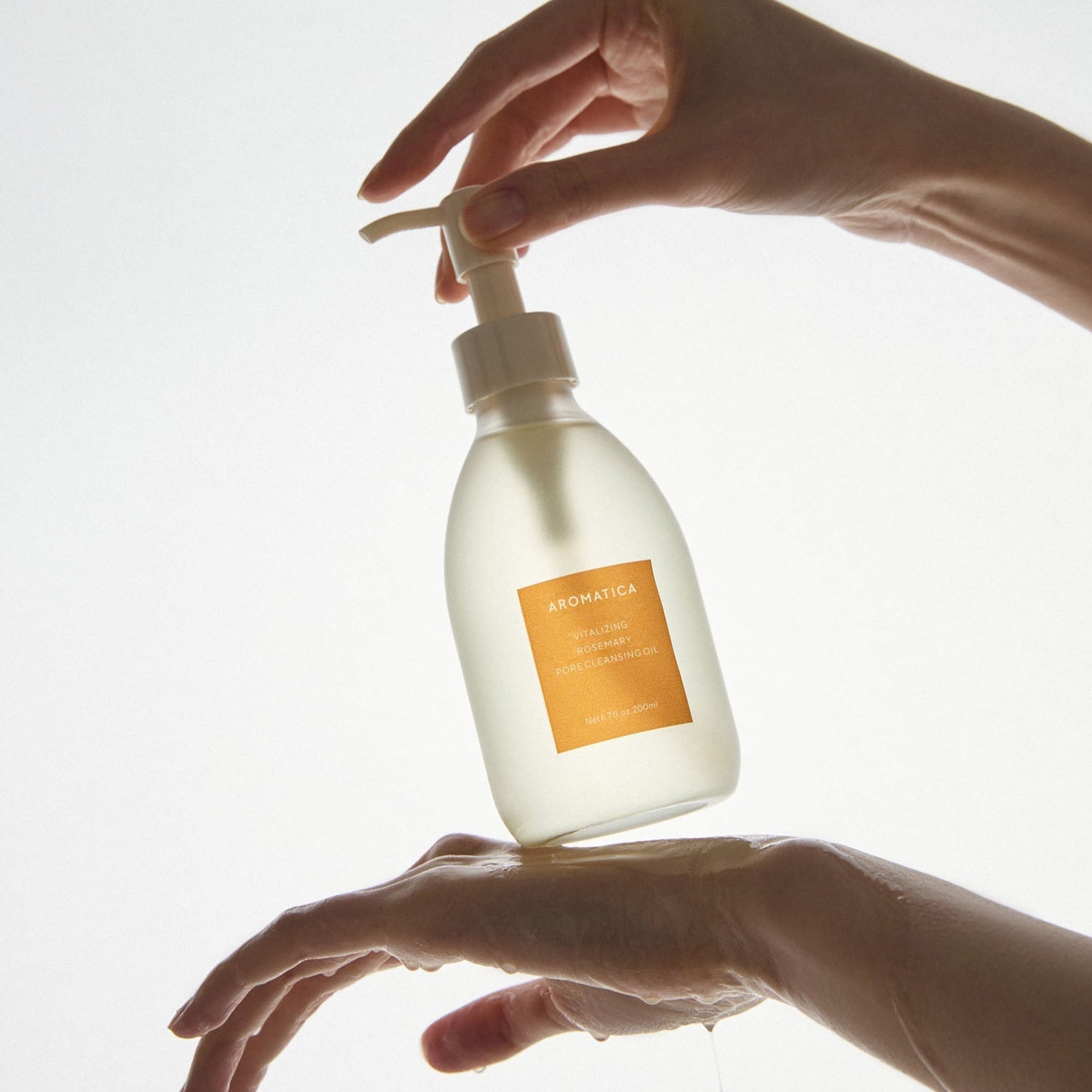 Hands using AROMATICA Vitalizing Rosemary Pore Cleansing Oil 200ML pump bottle
