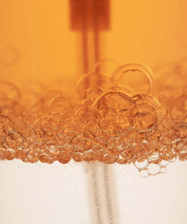 Close-up of AROMATICA Replenishing Hair Mist Jasmine & Vetiver 100ml with bubbles in orange liquid.