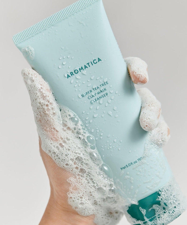 Hand holding AROMATICA Super Tea Tree Clay Mask Cleanser 150ML with foaming bubbles