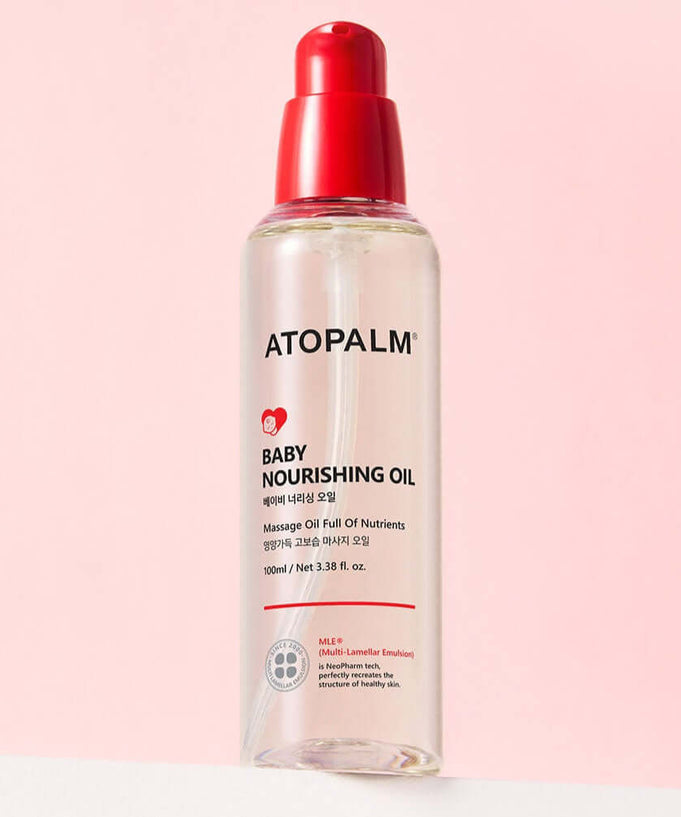 ATOPALM Baby Nourishing Oil 100ml bottle against a pink background, featuring a red cap, designed for gentle baby skin care.