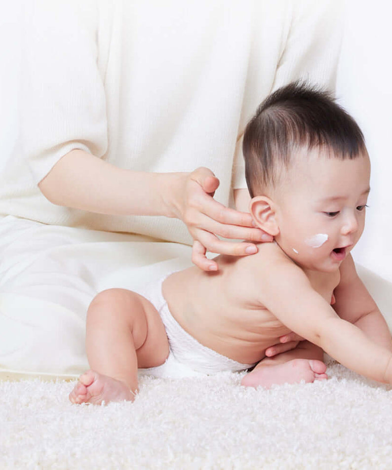 Baby with ATOPALM Panthenol Cream on face sitting with parent, showcasing moisturizing application.