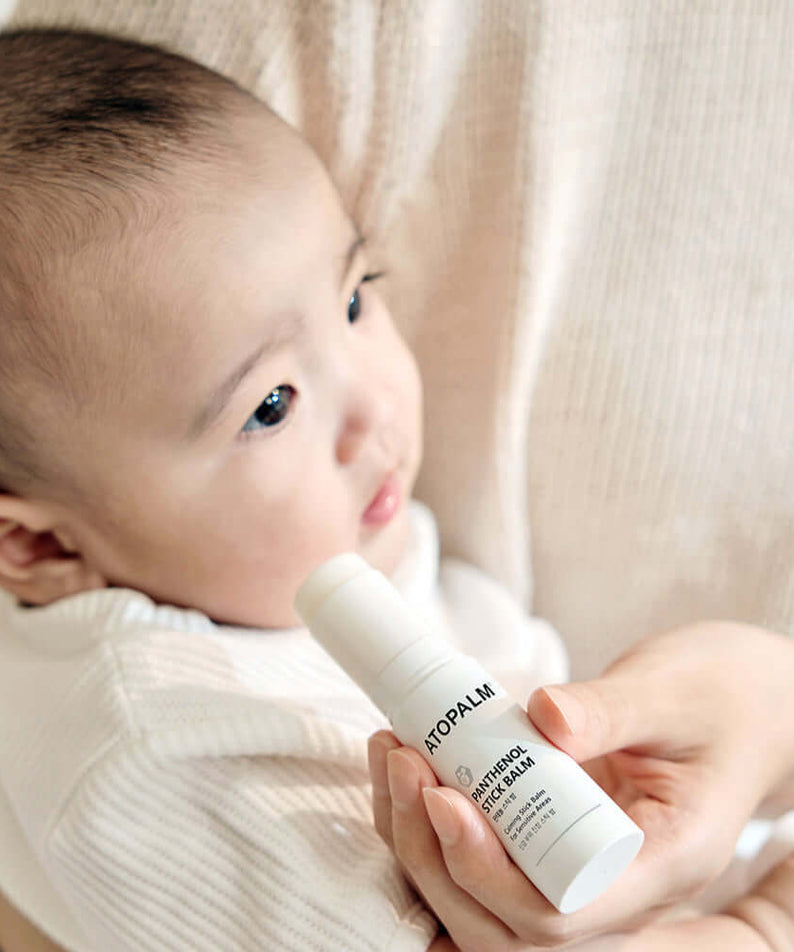 Person holding ATOPALM Panthenol Stick Balm 10g near a baby.
