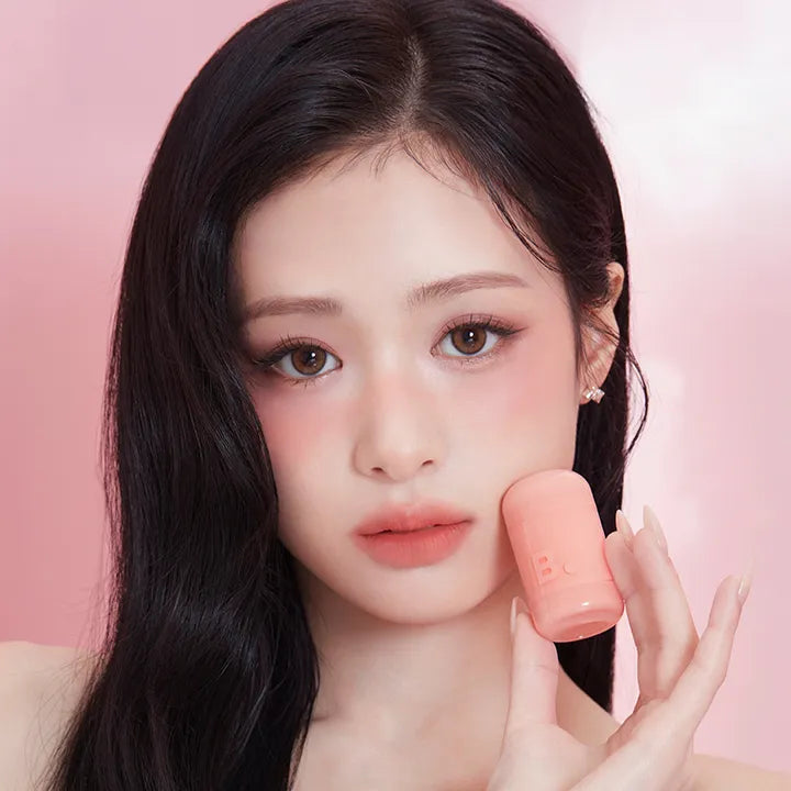 Woman holding BANILA CO Romantic Blush Lip & Cheek, showing makeup results on her face.