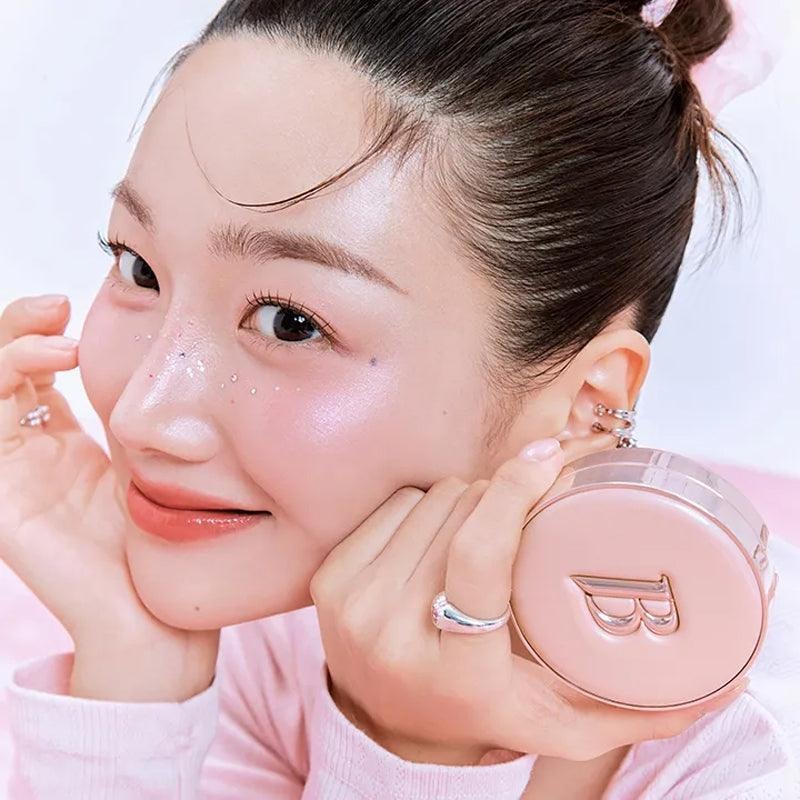 Smiling woman holding BANILACO Essence Skin Pink Cushion with glowing skin.