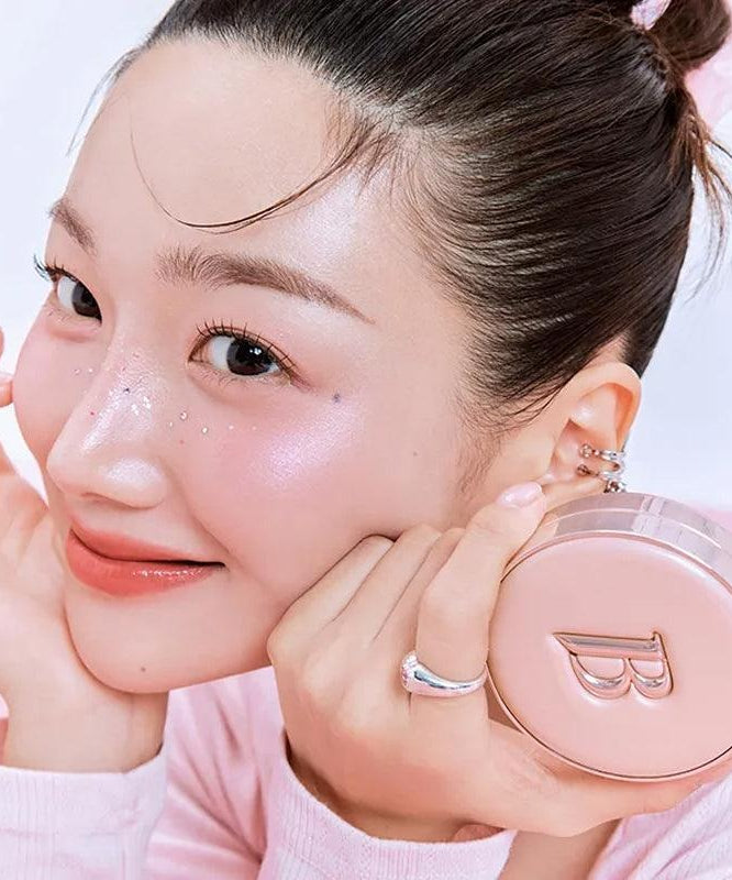 Smiling woman holding BANILACO Essence Skin Pink Cushion with glowing skin.