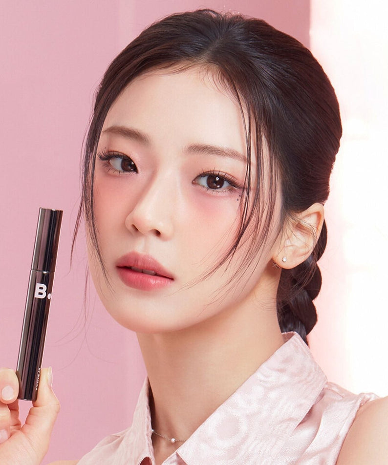 Model holding BANILACO Powerproof Mascara with sleek design and vibrant makeup, showcasing beauty and elegance.