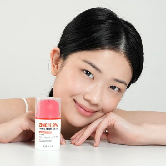 Woman smiling with BARULAB Zinc 11.9 Percent Trouble Rescue Cream in front, highlighting skincare benefits for trouble-prone skin.
