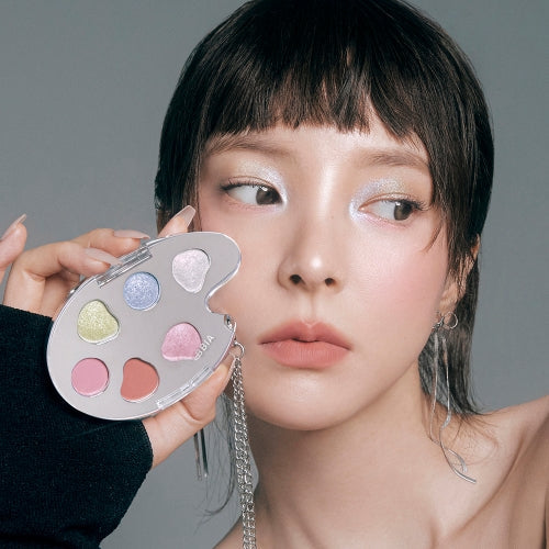 Close-up of woman holding BBIA Last Eye Palette with colorful eye shadows and subtle makeup look.