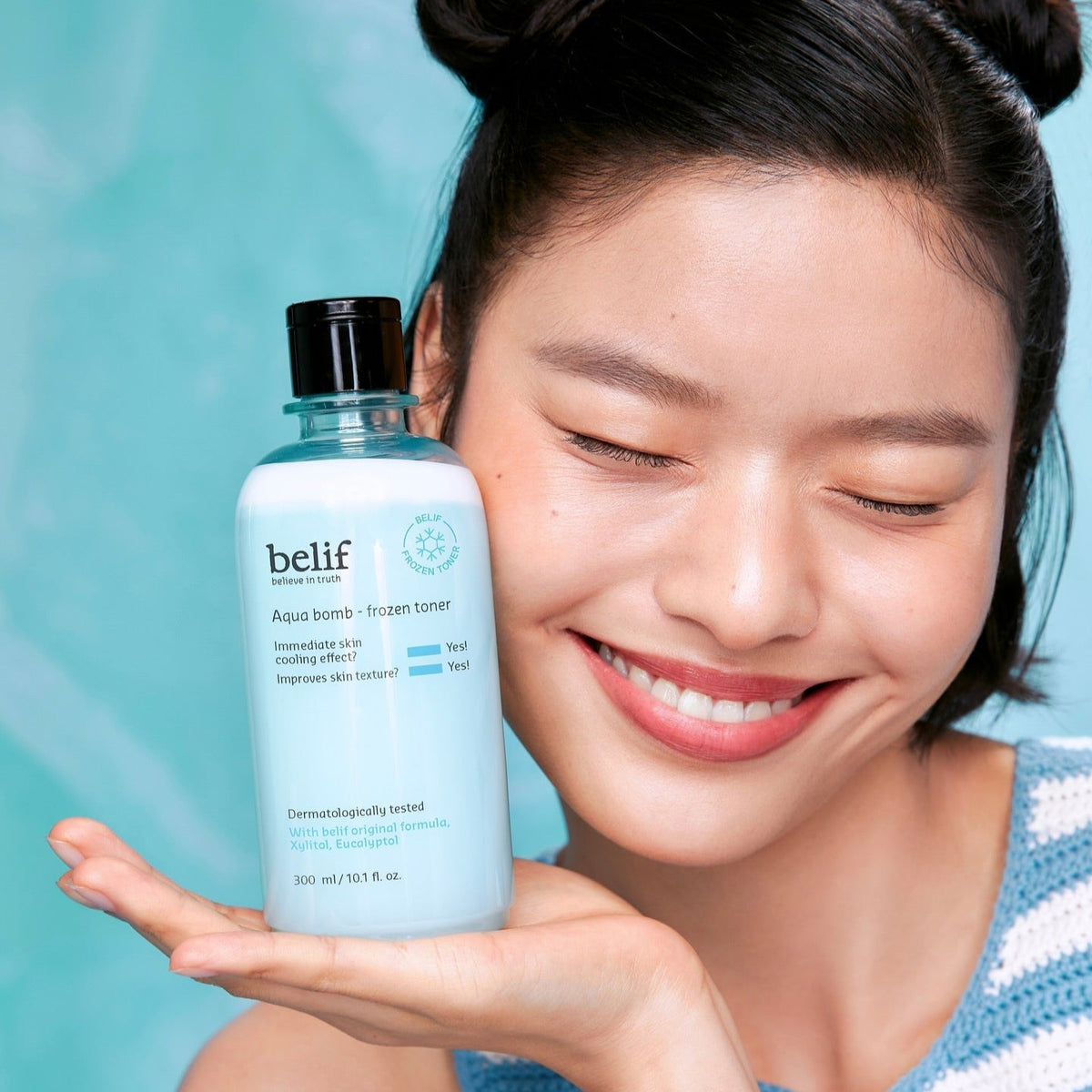Woman holding BELIF Aqua Bomb Frozen Toner 330ml with a blue background.