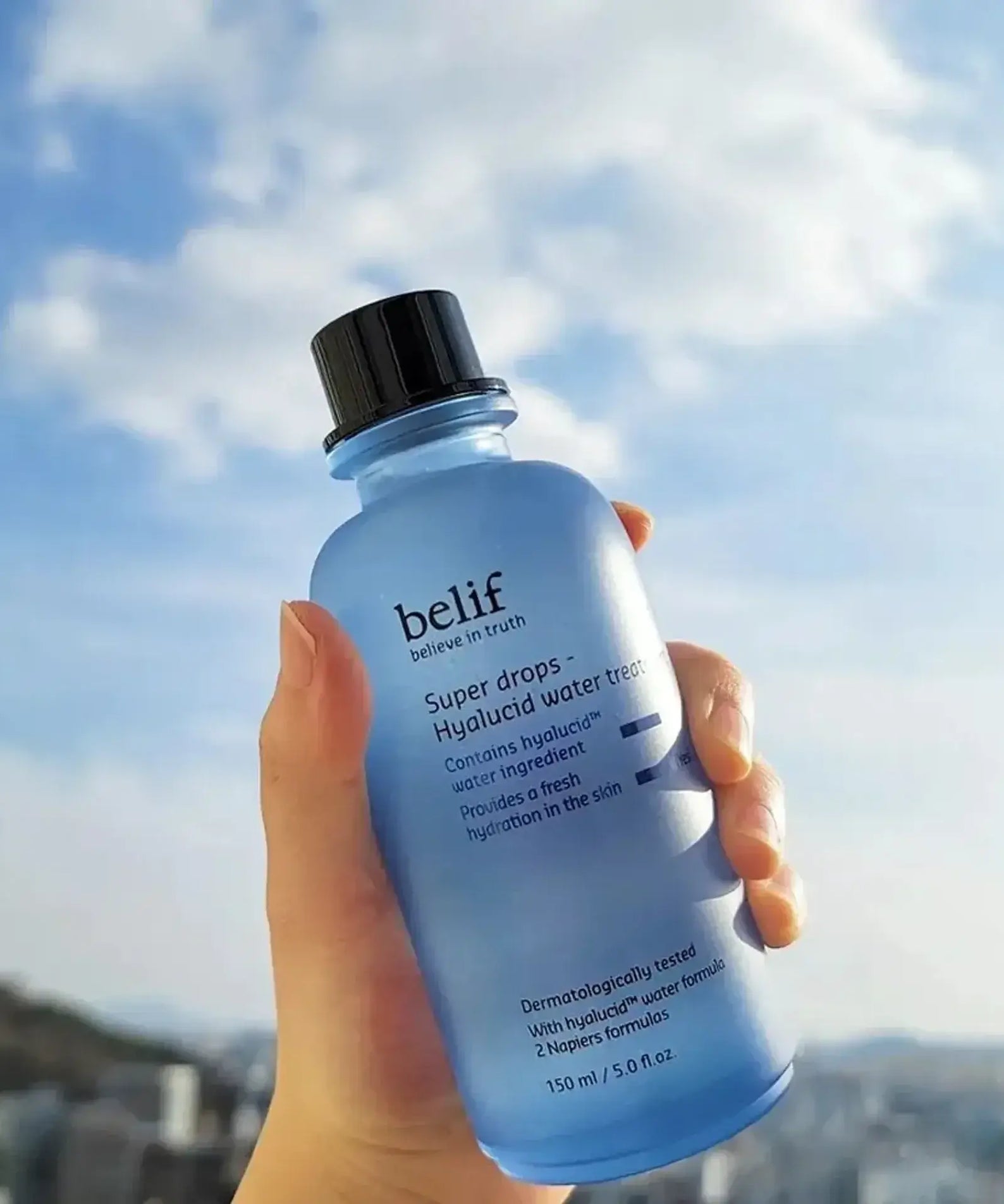 BELIF Super Drops-Hyalucid Water Treatment 150ml bottle held against a cloudy sky background